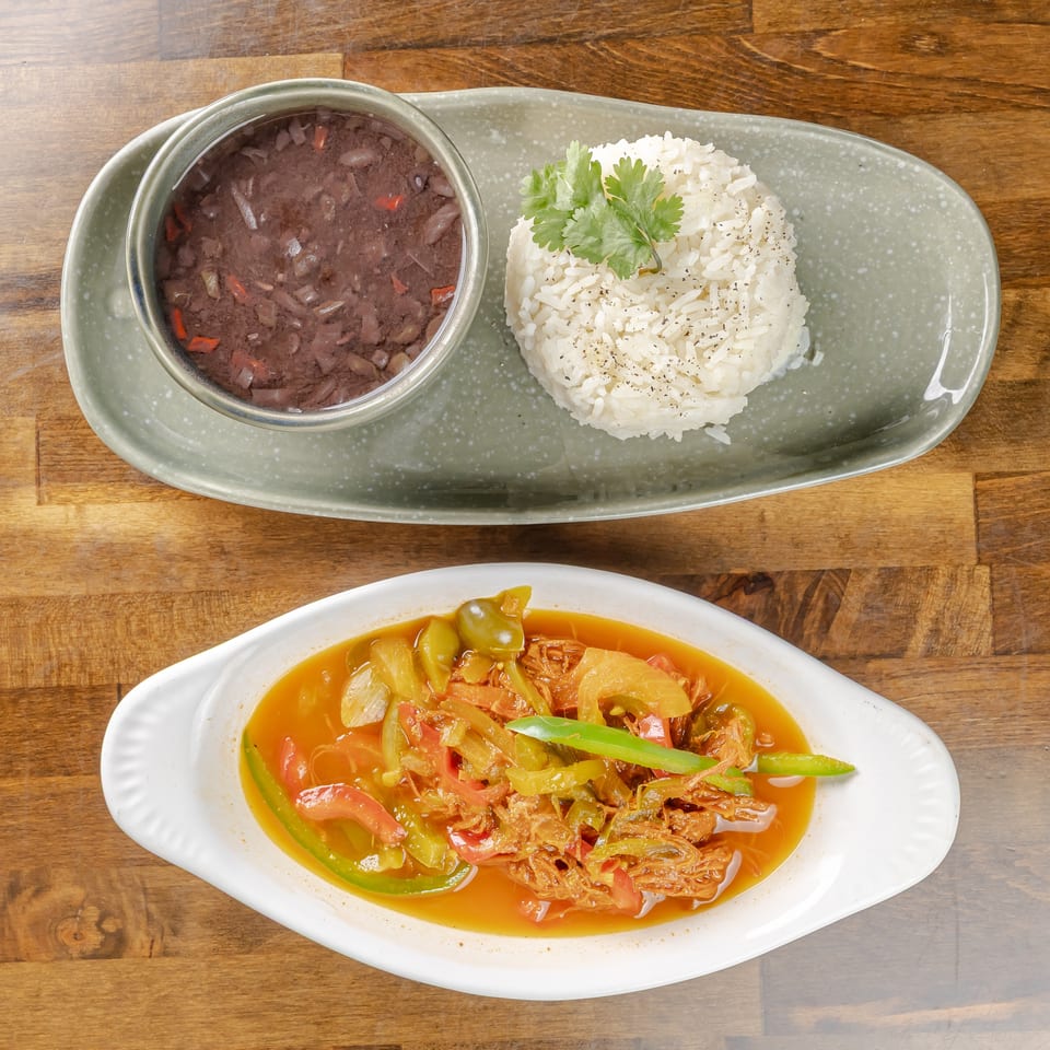 Rice topped with cilantro served beside black beans and a colorful vegetable stew on plates over a wooden table.