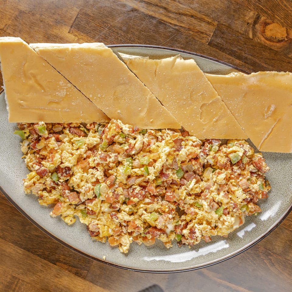 Scrambled eggs with bacon, tomatoes, peppers, and onions served on a platter with sliced flatbread.
