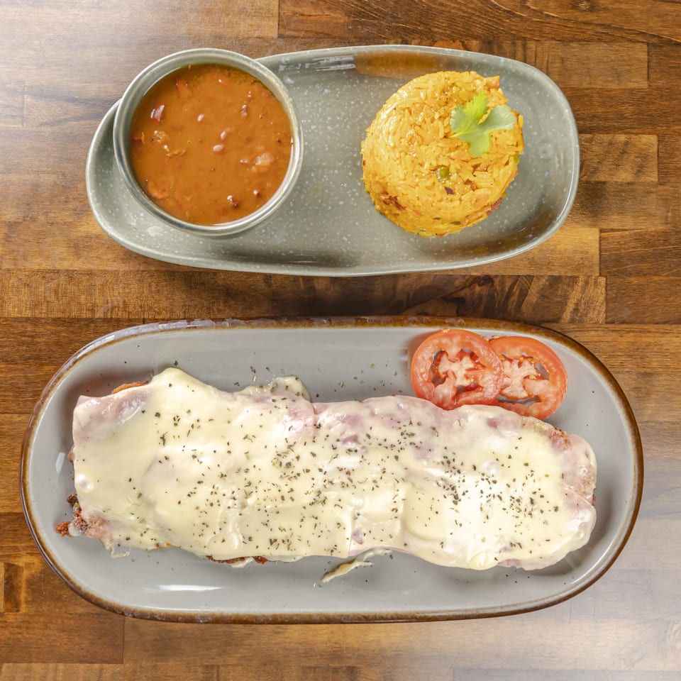 Top-down view of cheesy ham-and-tomato topped dish with yellow rice, brown sauce, and cilantro on plates.
